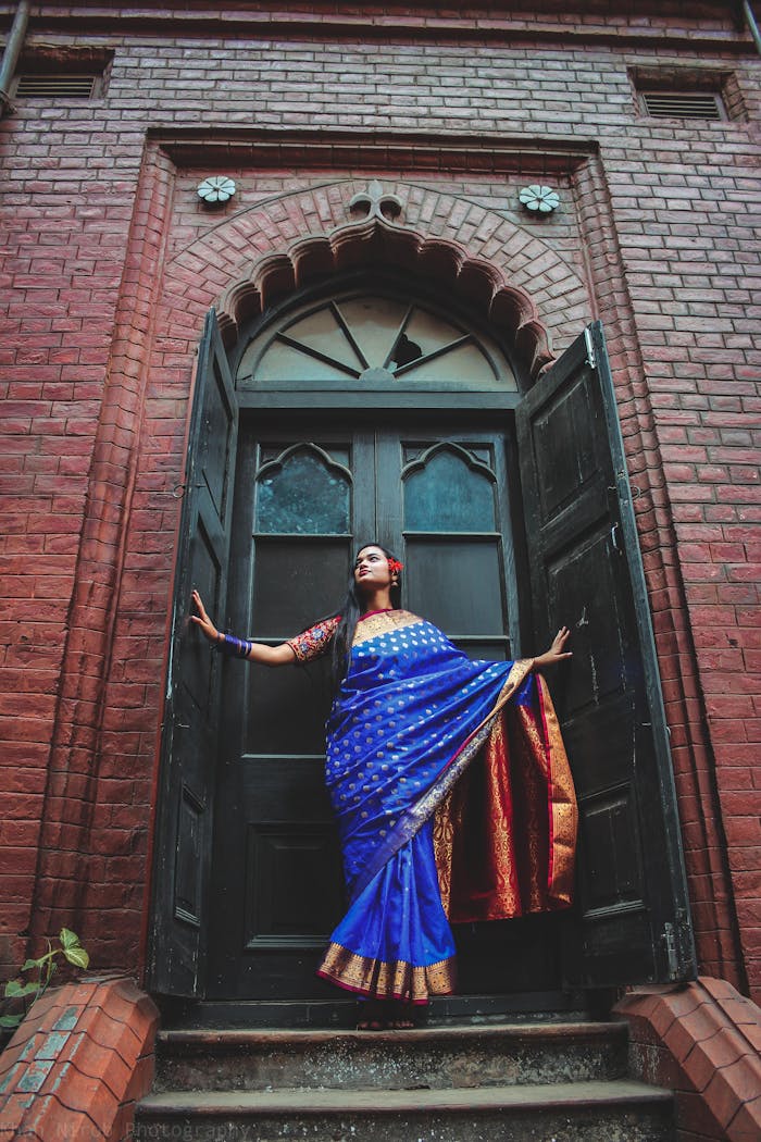 A woman in a vibrant saree poses dramatically in front of a historic wooden door.